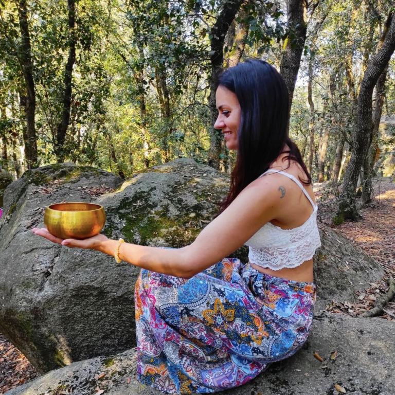 Conciencia de corazón Mujer sentada en una roca sosteniendo un cuenco dorado en un bosque.