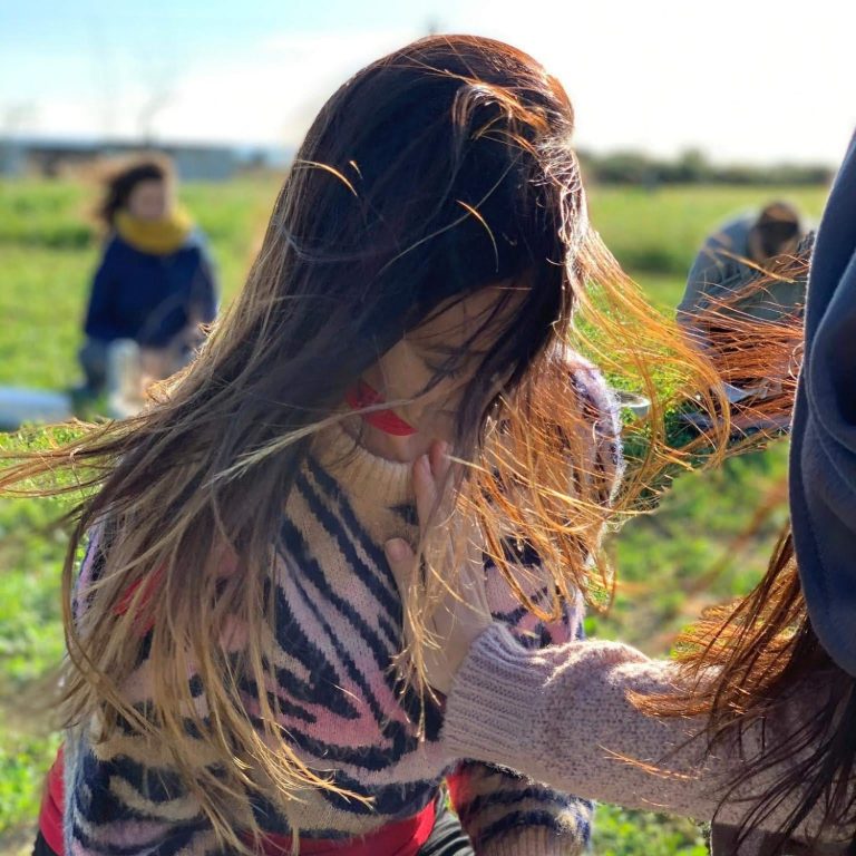 Una mujer con cabello largo y suelto, agachada en un campo al aire libre.