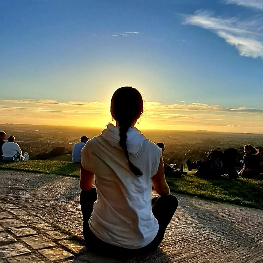 Meditación y meditación canalizada - Conciencia de corazón Persona sentada mirando un atardecer sobre un paisaje montañoso.