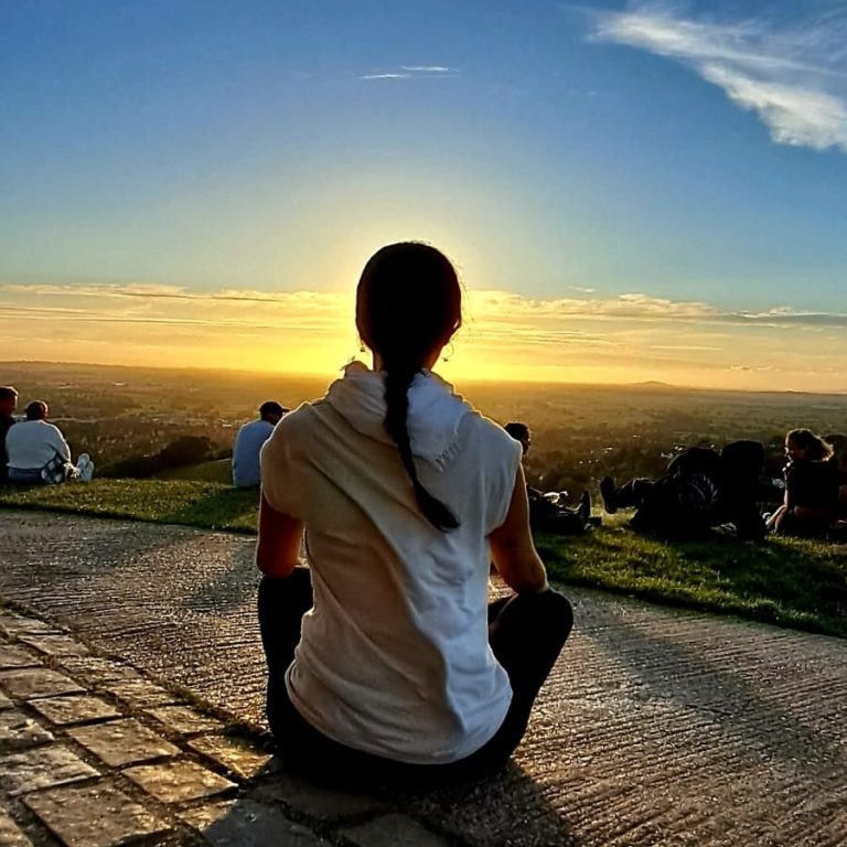 Persona sentada al atardecer, observando un paisaje con otras personas al fondo.