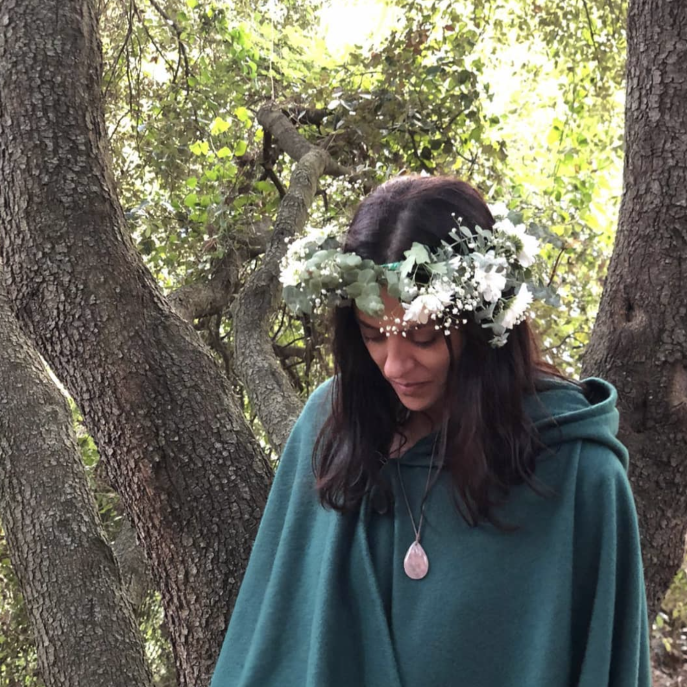Limpieza energética - conciencia de corazón Mujer con corona de flores y sudadera, mirando hacia abajo entre árboles.